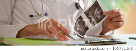 Female doctor working with ultrasound results of patients at her working desk. Female doctor working with ultrasound results of patients at her working desk. 105751108