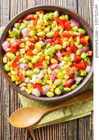 Vegetable salad with edamame beans, bell peppers, corn, tomatoes and onions close-up in a bowl. Vertical top view Vegetable salad with edamame beans, bell peppers, corn, tomatoes and onions close-up in a bowl. Vertical top view 105752544