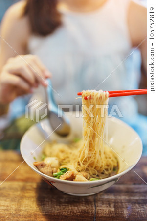 Woman eating Thai Boat noodle thicken soup with Pork, balls, crispy fried pork skin, basil leaf and Vegetables. Traditional and Famous Street food in Thailand Woman eating Thai Boat noodle thicken soup with Pork, balls, crispy fried pork skin, basil leaf and Vegetables. Traditional and Famous Street food in Thailand 105752819