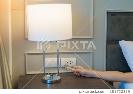 Woman hand turning on or turning off switch the minimal lamp in modern bedroom. Apartment living concept Woman hand turning on or turning off switch the minimal lamp in modern bedroom. Apartment living concept 105752829