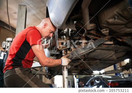 Professional worker, repairman changing car wheel, fixing problem. Hardworking, strong man working in auto, servicing center. Concept of repairing, maintaining car. Professional worker, repairman changing car wheel, fixing problem. Hardworking, strong man working in auto, servicing center. Concept of repairing, maintaining car. 105753211