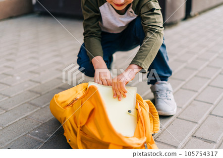 Back to school. Cute child packing backpack, holding notepad and training books going to school. Boy pupil with bag. Elementary school student going to classes. Kid walking outdoor on the city street 105754317