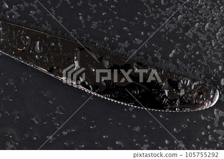 a steel knife covered with water droplets on black paper 105755292