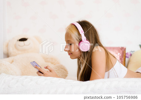 Teenager with headphones listens to music in bed, communicates on social networks in the morning after sleep Teenager with headphones listens to music in bed, communicates on social networks in the morning after sleep 105756986