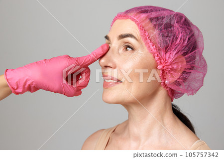 Profile elderly lady getting preparing for plastic surgery procedures by doctor touching her chin in pink gloves. 105757342