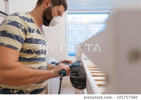man rubs wooden child bed with power sander or grinder removing old paint man rubs wooden child bed with power sander or grinder removing old paint 105757360