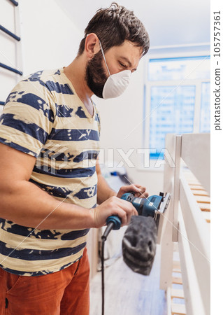 man rubs wooden child bed with power sander or grinder removing old paint man rubs wooden child bed with power sander or grinder removing old paint 105757361