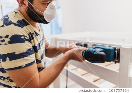 man rubs wooden child bed with power sander or grinder removing old paint man rubs wooden child bed with power sander or grinder removing old paint 105757364
