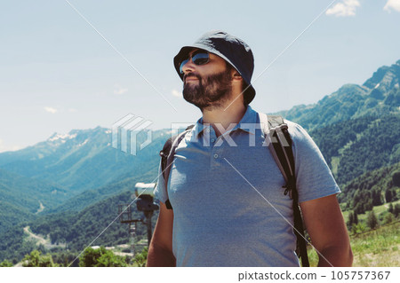 millenial bearded tourist man wearing bucket hat, with backpack trekking in mountains 105757367