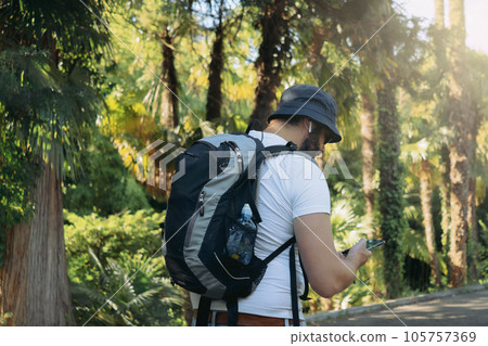 millenial bearded tourist man wearing bucket hat, with backpack and earpods using smartphone for navigation 105757369