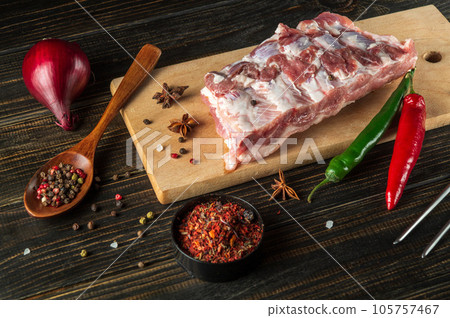 Raw pork ribs on a cutting board with spices and seasonings. Preparing to cook delicious food for a restaurant Raw pork ribs on a cutting board with spices and seasonings. Preparing to cook delicious food for a restaurant 105757467