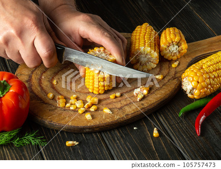 The cook cuts corn with a knife. Maize is an excellent dietary breakfast or lunch with vegetables. Working environment at the restaurant kitchen table 105757473