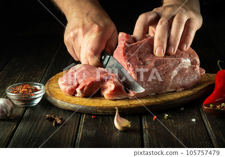 The chef cuts a raw beef steak with a knife on a wooden cutting board. The concept of the process of cooking a meat dish with aromatic spices The chef cuts a raw beef steak with a knife on a wooden cutting board. The concept of the process of cooking a meat dish with aromatic spices 105757479
