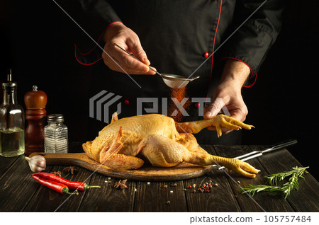Professional chef prepares raw chicken in the kitchen. The cook adds paprika to the rooster before frying. Preparing to fry fried chicken 105757484
