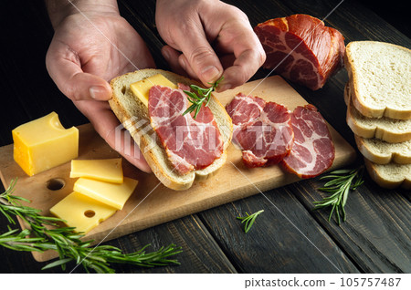 The cook's hands make a sandwich and add rosemary. Delicious fast food idea The cook's hands make a sandwich and add rosemary. Delicious fast food idea 105757487