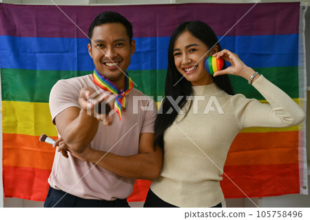 Beauty blogger and trans gender influencer standing against LGBTQ rainbow flag and smiling to camera Beauty blogger and trans gender influencer standing against LGBTQ rainbow flag and smiling to camera 105758496