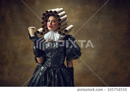 Portrait of woman with bright makeup in paper tube wig dressed in black dress made of garbage bags holding disposable coffee cup. Portrait of woman with bright makeup in paper tube wig dressed in black dress made of garbage bags holding disposable coffee cup. 105758550