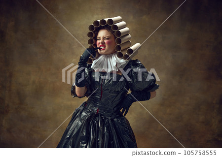 Portrait of woman with paper tube wig in black dress made of garbage bags brushing teeth with gloved hands against vintage background. 105758555