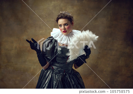 Photoshoot of woman in ball dress made of garbage bags and fan in hand over vintage background. Portrait of posing aristocratic women. Photoshoot of woman in ball dress made of garbage bags and fan in hand over vintage background. Portrait of posing aristocratic women. 105758575