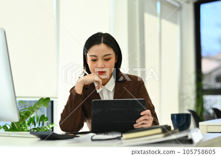 Focused asian woman entrepreneur using digital tablet working on investment and marketing projects at office Focused asian woman entrepreneur using digital tablet working on investment and marketing projects at office 105758605