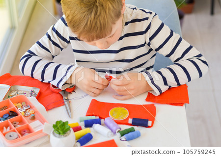 Close-up of a beautiful 9-year-old Caucasian boy who studies to sew with a needle and thread. Close-up of a beautiful 9-year-old Caucasian boy who studies to sew with a needle and thread. 105759245