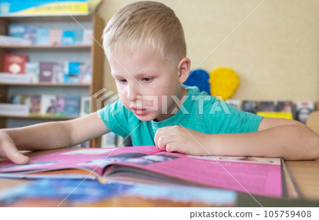 Boy in library. Seven year Ukrainian guy is sitting at a table in library and reading book. Concept of normal learning, thirst for knowledge, desire to learn new things. Blurred background and letters Boy in library. Seven year Ukrainian guy is sitting at a table in library and reading book. Concept of normal learning, thirst for knowledge, desire to learn new things. Blurred background and letters 105759408