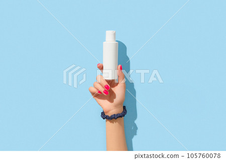 Womans hand holding white cream bottle on blue background. Body care beauty treatment concept 105760078
