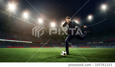 Emotional businessman hitting football ball on 3d arena with flashlights. Earning money during match Emotional businessman hitting football ball on 3d arena with flashlights. Earning money during match 105761325