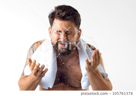 Morning get ready. Bearded shirtless man with towel on shoulders, washing face against white studio background 105761378