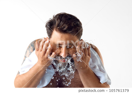 Morning get ready. Bearded shirtless man with towel on shoulders, washing face against white studio background 105761379
