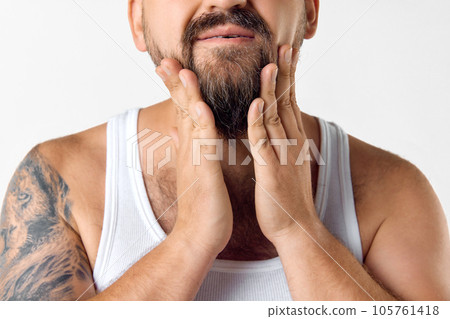 Cropped image of man taking care after beard with cosmetics, applying gel, wax, oil against white studio background 105761418