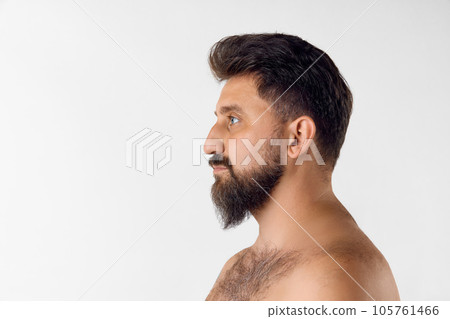 Side view of bearded man looking straight, posing shirtless against white studio background. Barber care 105761466