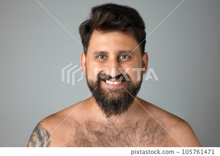 Smiling, mature, bearded man with blue eyes standing shirtless, looking at camera against grey studio background 105761471