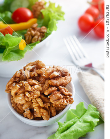Green salad with walnuts. Walnuts in plate are on table. Top view. Still life. 105762392