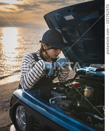 A girl who opens the bonnet at sunset and looks into it to maintain it 105762970
