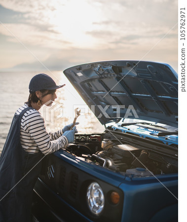 A girl in profile who is trying to open the hood at sunset and maintain 105762971