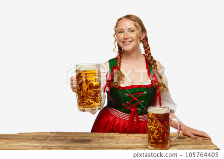Smiling young girl wearing traditional Bavarian or german dirndl, holding huge beerglasses over white background. Concept of Oktoberfest. 105764405