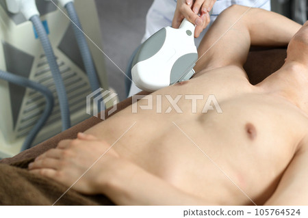 Therapist and male patient performing armpit hair removal treatment 105764524
