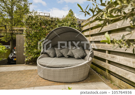 an outdoor area with a wicker chair and some pillows on the ground in front of a wooden fence behind it an outdoor area with a wicker chair and some pillows on the ground in front of a wooden fence behind it 105764936