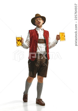 Young attractive mustache man in hat, wearing folk Bavarian outfit, holding beer mug walking and singing over white background. Oktoberfest concept Young attractive mustache man in hat, wearing folk Bavarian outfit, holding beer mug walking and singing over white background. Oktoberfest concept 105764937