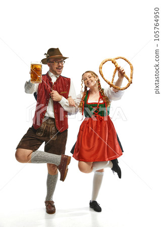 Two genial friends. Full lenght portrait of emotional man and woman wearing folk festival outfits with Bavarian beer glasses and huge pretzel. Two genial friends. Full lenght portrait of emotional man and woman wearing folk festival outfits with Bavarian beer glasses and huge pretzel. 105764950