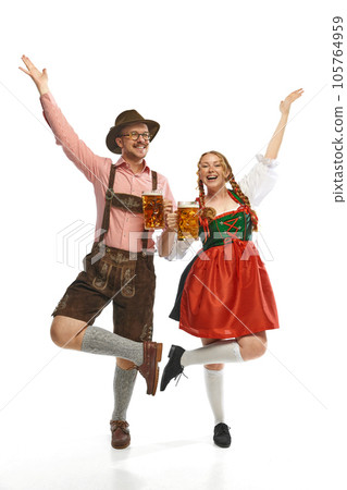 Two dancing friends. Full lenght portrait of emotional man and woman wearing folk festival outfits with Bavarian beer glasses. 105764959