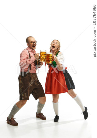 Two cheerful friends. Full lenght portrait of emotional man and woman wearing folk festival outfits with Bavarian beer glasses. 105764966