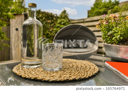 a bottle and glass sitting on top of a table with flowers in the back ground next to an outdoor grill a bottle and glass sitting on top of a table with flowers in the back ground next to an outdoor grill 105764971