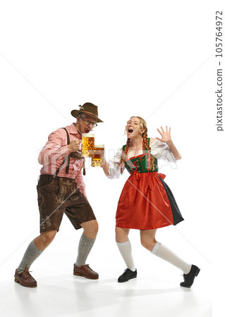 Two celebrating friends. Shouting man and woman wearing traditional German outfits, having clinking glasses with Bavarian beer. Two celebrating friends. Shouting man and woman wearing traditional German outfits, having clinking glasses with Bavarian beer. 105764972