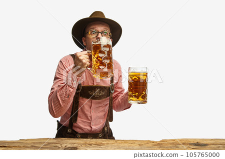 Portrait of young cheerful man in hat, wearing folk Bavarian clothes, drinking beer isolated white background. Concept of Oktoberfest 105765000