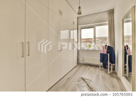 a walk - in closet with clothes hanging on the wall and an open door that leads to a bathroom area 105765001