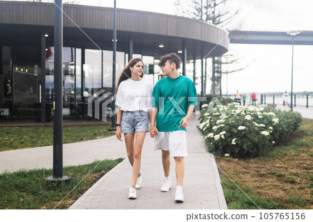 two young people are walking and talking in a city coastal park two young people are walking and talking in a city coastal park 105765156
