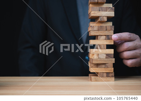 Businessman hand of businessman pulling out or placing wood block on the tower with copyspace. Business risk, strategy and planing concept idea. Businessman hand of businessman pulling out or placing wood block on the tower with copyspace. Business risk, strategy and planing concept idea. 105765440