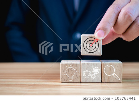 Businessman holding a wooden block that prints target icon. Business concept. Management concept. Business planning concept. Businessman holding a wooden block that prints target icon. Business concept. Management concept. Business planning concept. 105765441